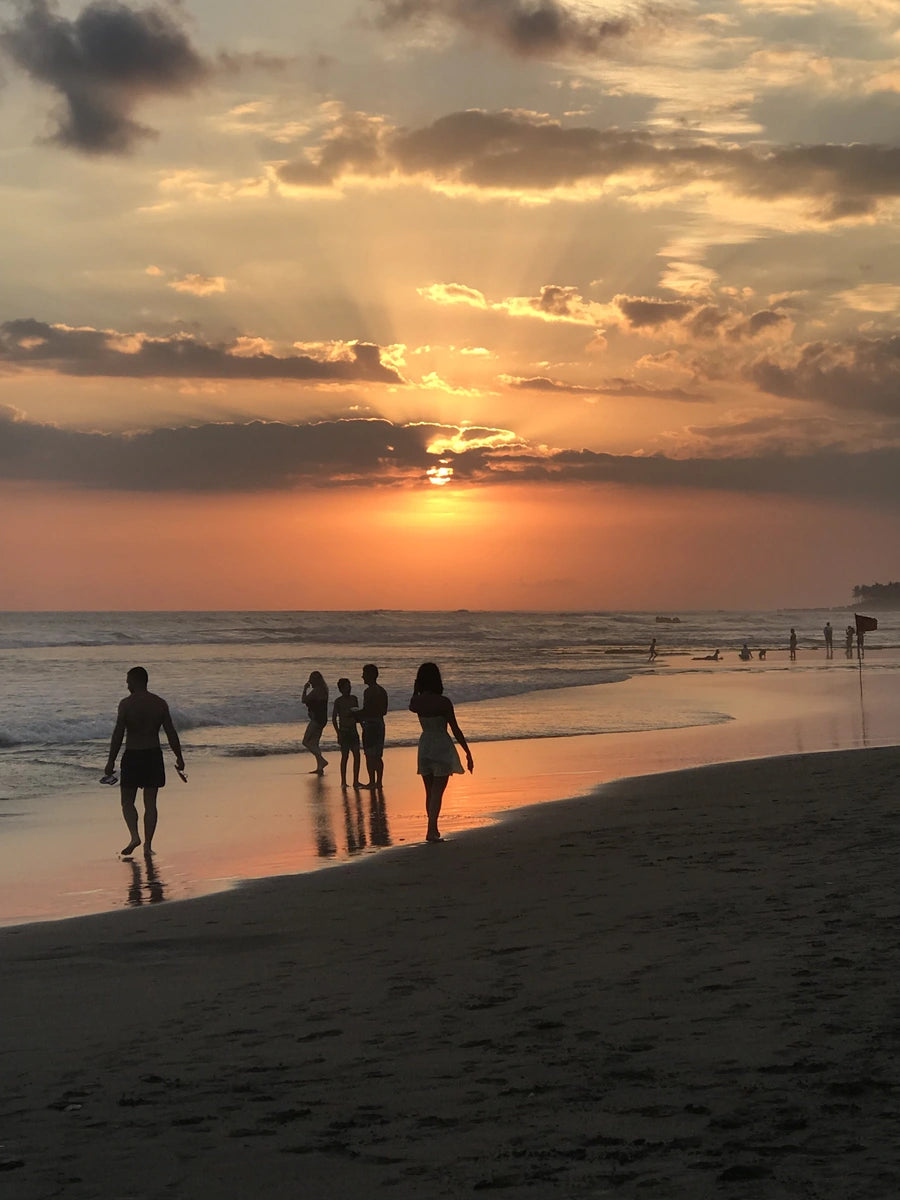 A family of tourists on holiday walk along a beach in Bali with a beautiful sunset on the horizon.