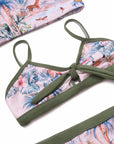 A close-up of a bikini top with a tropical floral print on a light pink base, featuring olive green trim and straps with a front tie detail.