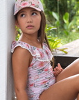 Girl wearing a pink Petal floral mesh cap and matching floral swimsuit in a garden.