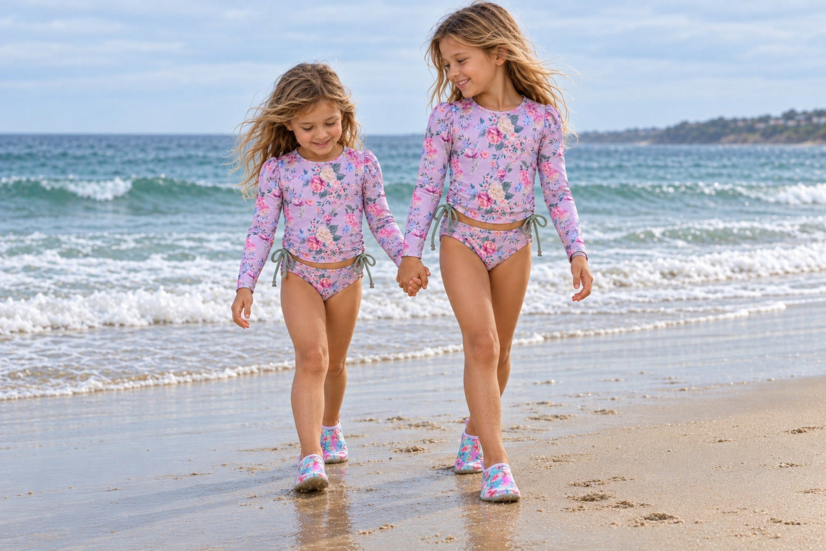 Two girls walking hand in hand along the beach in floral swimwear and Garden of Grace water shoes