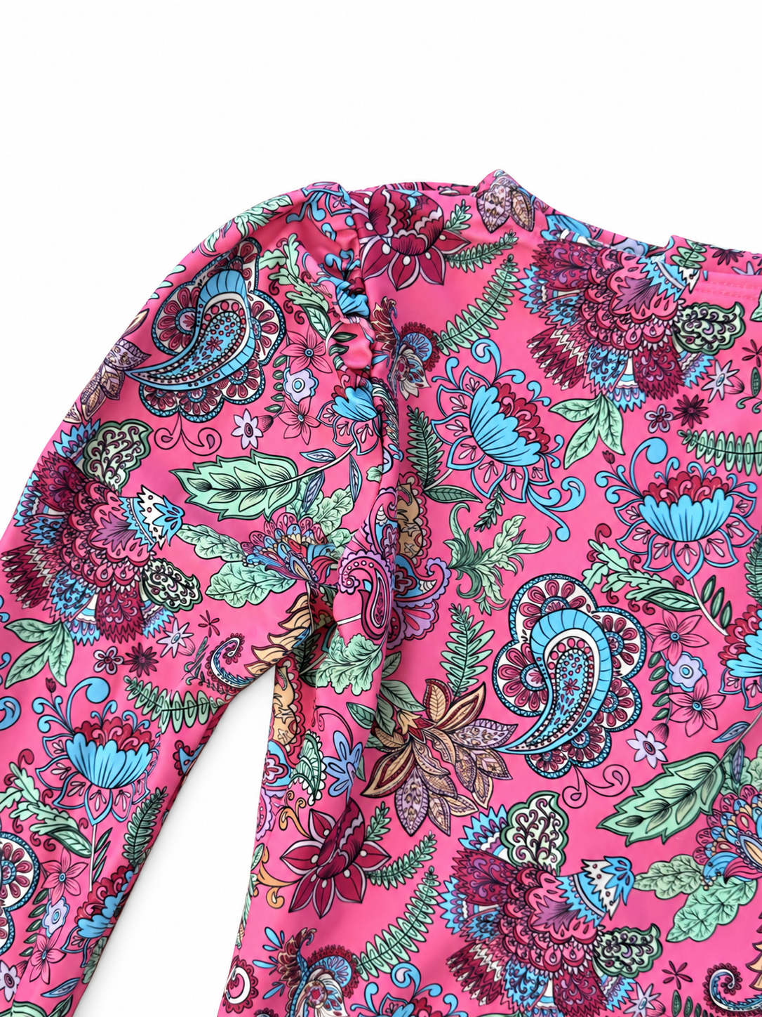 A close-up of a long-sleeve top featuring a vibrant pink base with a detailed paisley and floral print in teal, purple, green, and red.