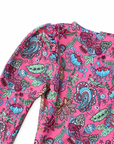 A close-up of a long-sleeve top featuring a vibrant pink base with a detailed paisley and floral print in teal, purple, green, and red.