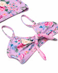 A pink floral bikini top with a tie-front detail, shown on a white background with a matching floral bikini bottom partially visible in the top left corner.