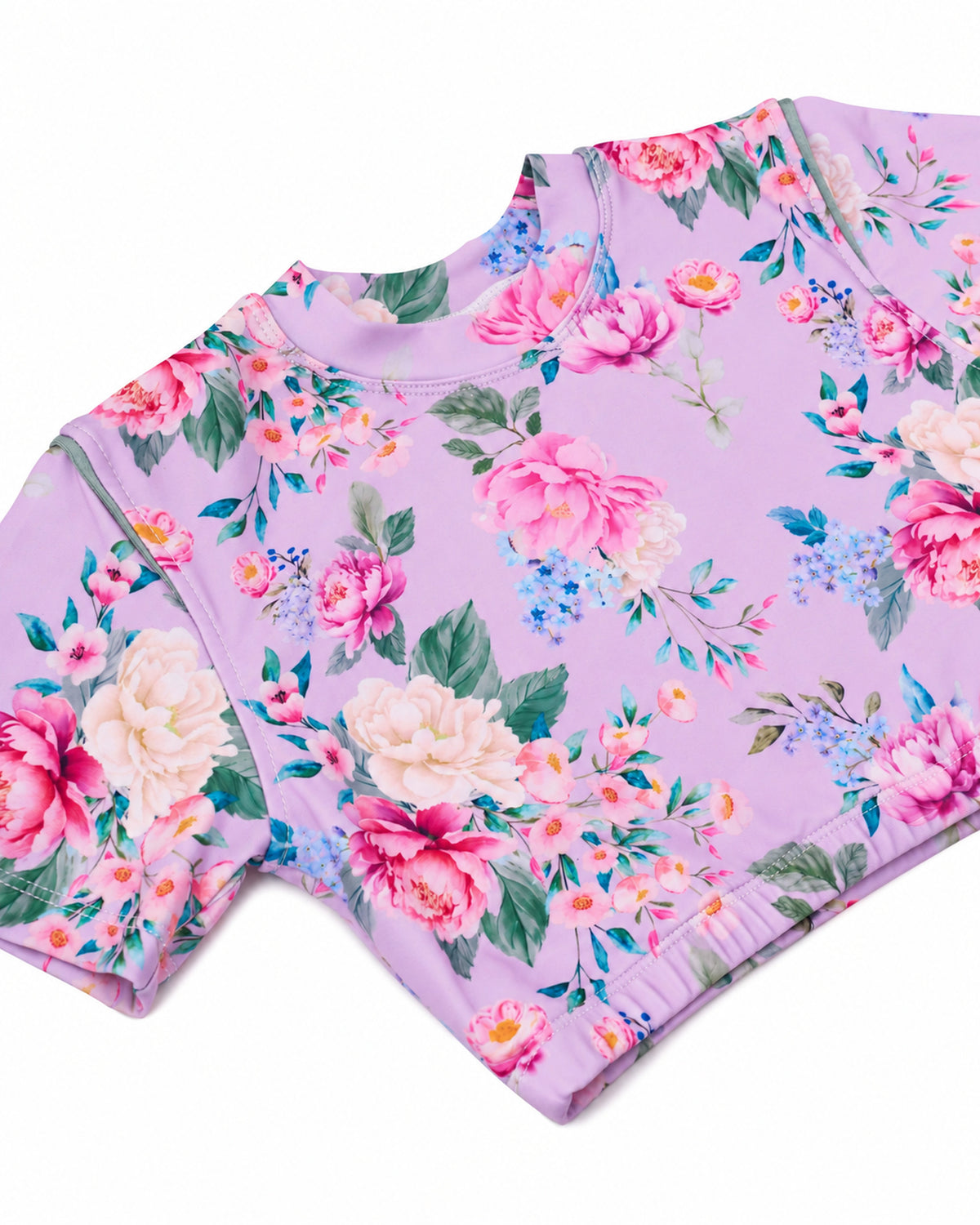 A short-sleeve rashie with a vibrant floral print on a light purple/lavender base, featuring pink, white, and blue flowers with green leaves.