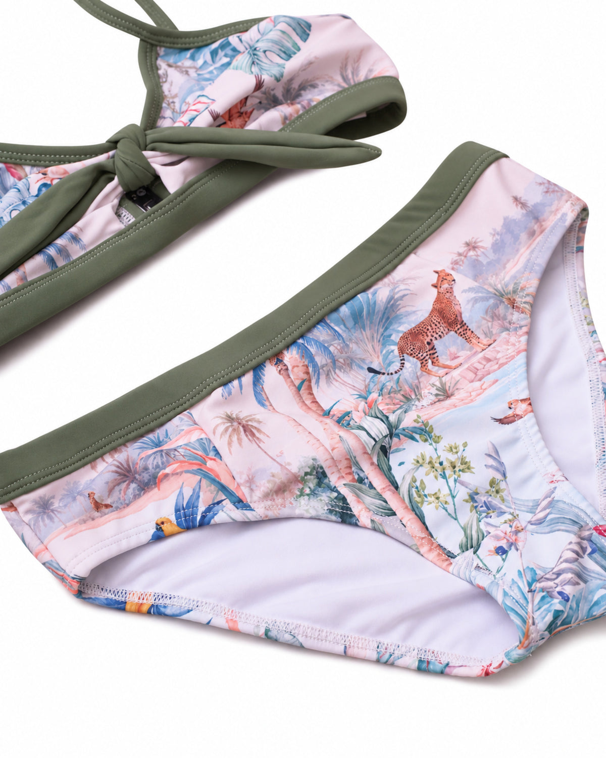 A close-up of a bikini bottom with a tropical safari print in pink, blue, and green, featuring olive green trim and a side tie on the top, shown on a white background.