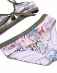 A close-up of a bikini bottom with a tropical safari print in pink, blue, and green, featuring olive green trim and a side tie on the top, shown on a white background.