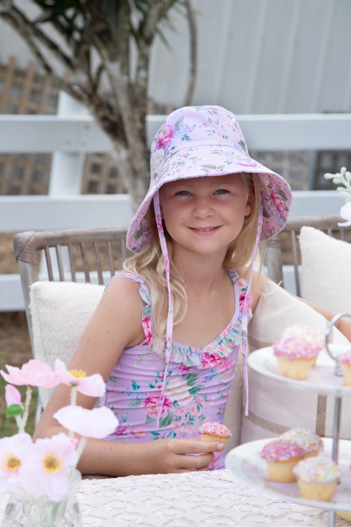 Girl wearing the Olga Valentine Violetta purple floral bucket hat with ties and matching swimwear, lifestyle photo