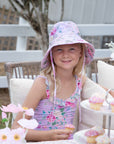 Girl wearing the Olga Valentine Violetta purple floral bucket hat with ties and matching swimwear, lifestyle photo